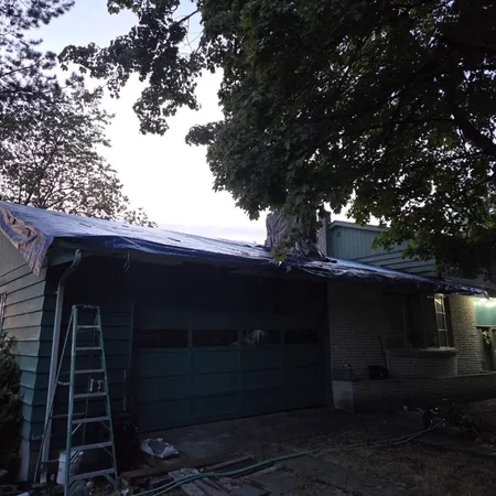 Dusk emergency tarping on a house with ladder against the wall