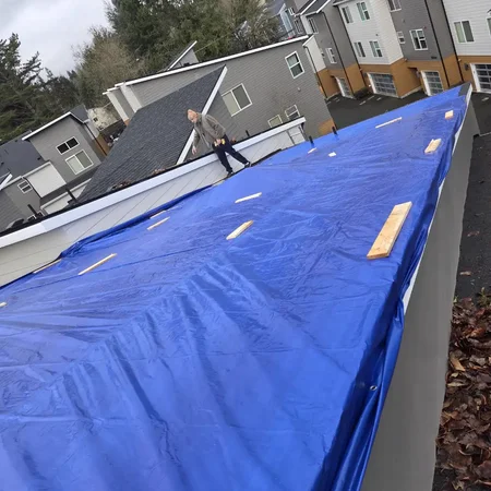 Crew securing blue tarp battens on a multifamily roof