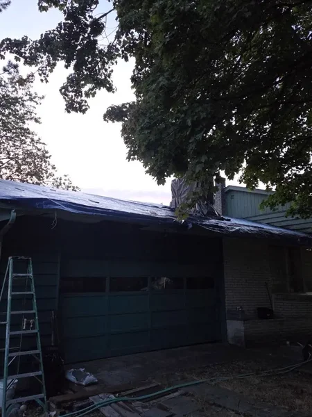 Dusk emergency tarping on a house with ladder against the wall
