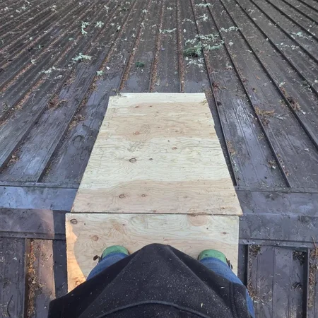 Plywood walk boards on a wet metal roof during emergency work