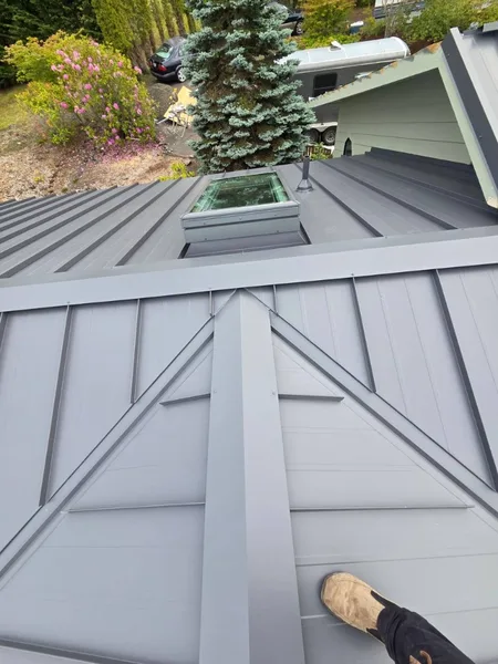 High-angle view of dark gray standing seam metal roof with plumbing vent flashing
