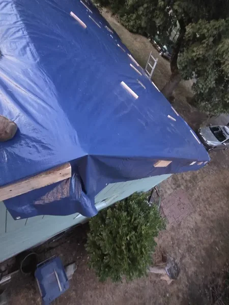 Blue emergency tarp secured with wooden battens on a residential roof edge
