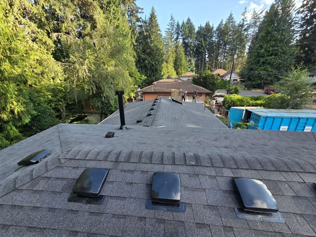 Residential shingle roof install crew and blue dumpster