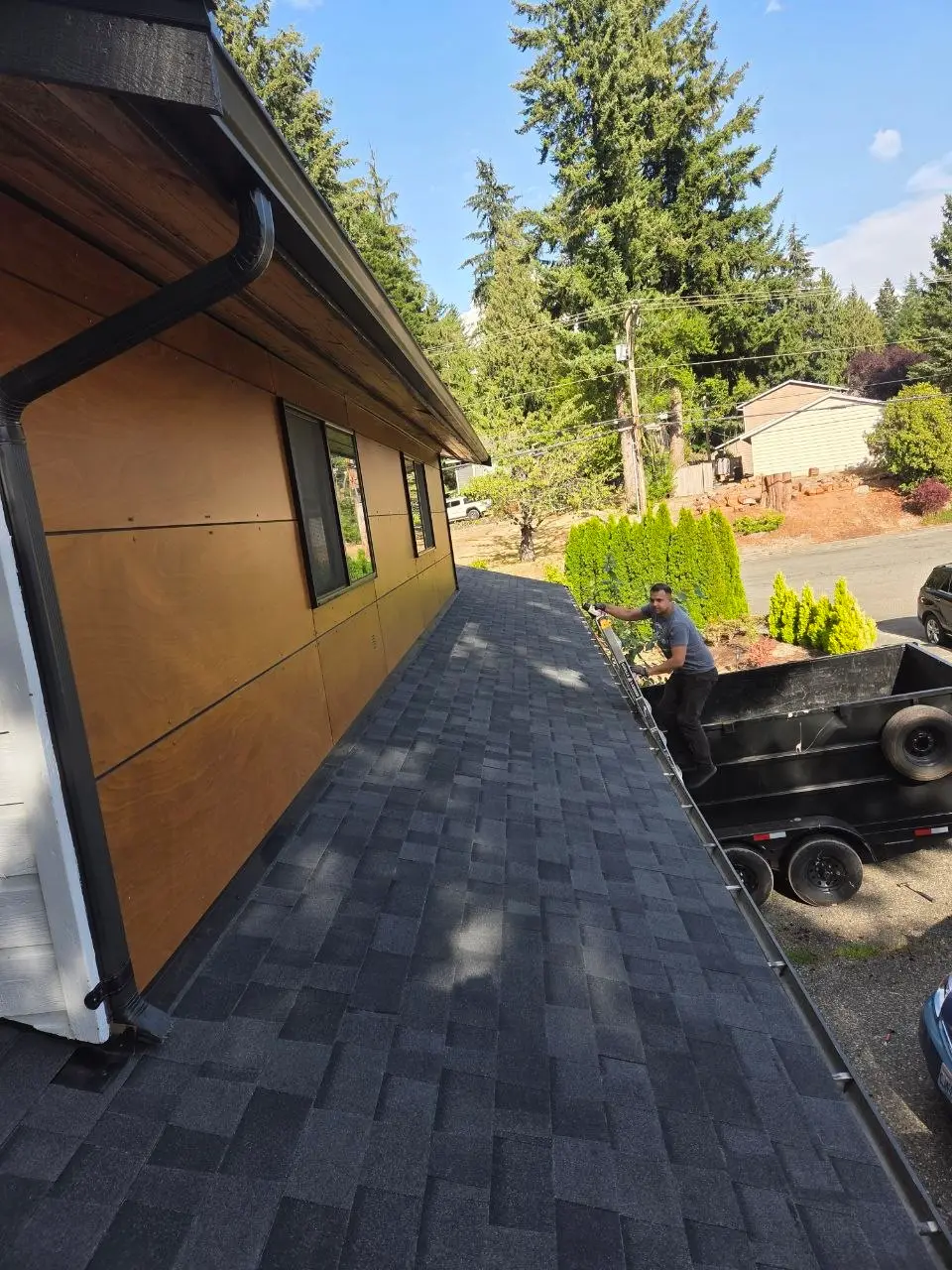 Shingle install with roofer on ladder and black gutters