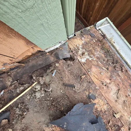 Rotted decking and torn underlayment at a wall corner