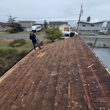 Open shingle deck after tear-off, with a crew member on the slope